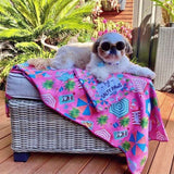 Small fluffy dog wearing sunglasses resting on the Salty Paws Designs Life's a Beach compact lightweight dog towel in pink on an outdoor lounger