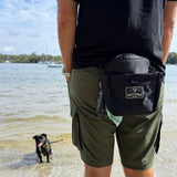 Salty Paws Original Dog Training Treat Pouch worn on hip at the beach with small black dog in background