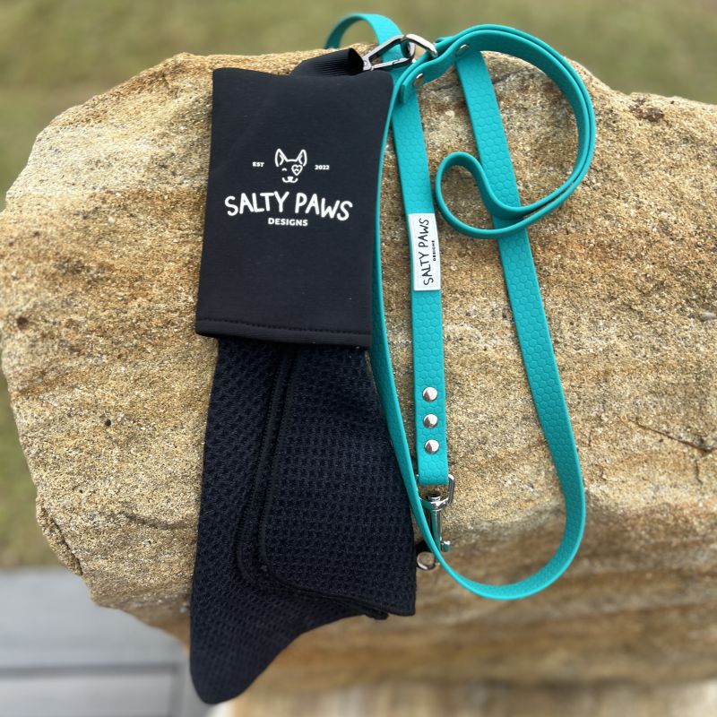 Salty Paws Slobber Towel next to a teal dog lead, laid on a rock outdoors