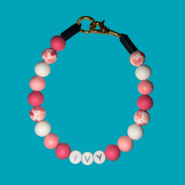 Bracelet with pink and white beads and 'IVY' charm on a blue background