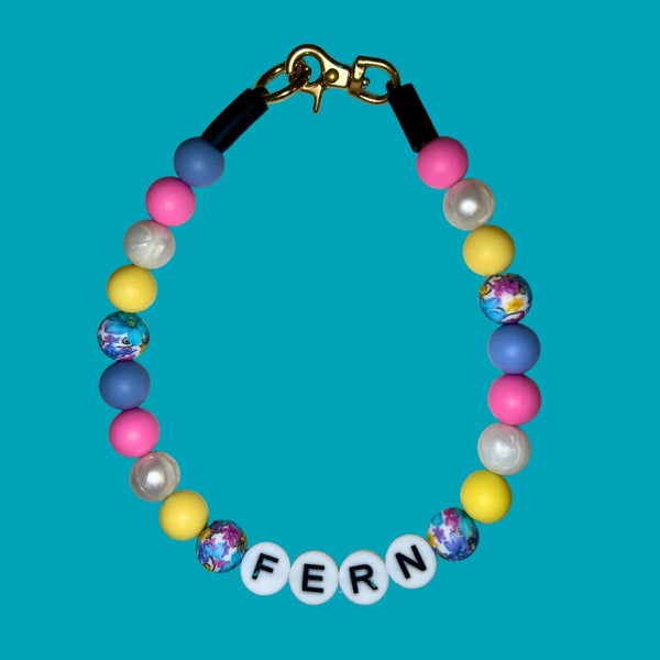 Colorful beaded bracelet with 'FERN' charm on a blue background