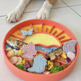 Sunset Slow Feeder in orange loaded with enrichment food and treats with dog paws visible